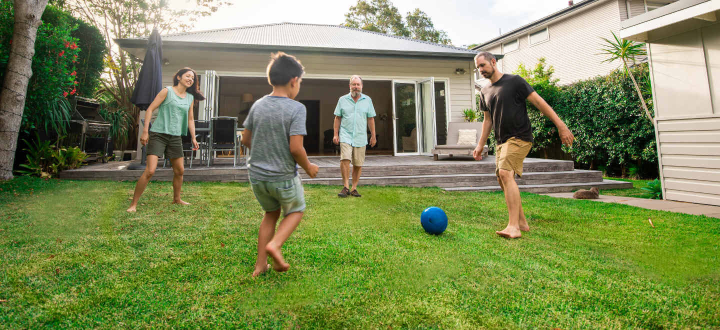 A family of four kicks around a ball in the backyard on a warm day.