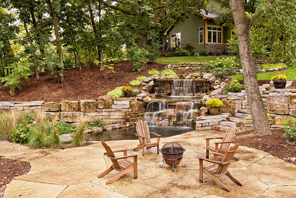Backyard - house in background, water feature prominent and fire pits with chairs