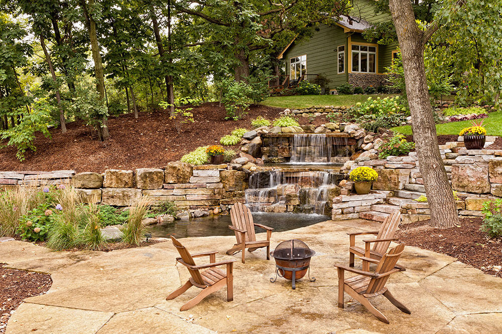 Backyard - house in background, water feature prominent and fire pits with chairs