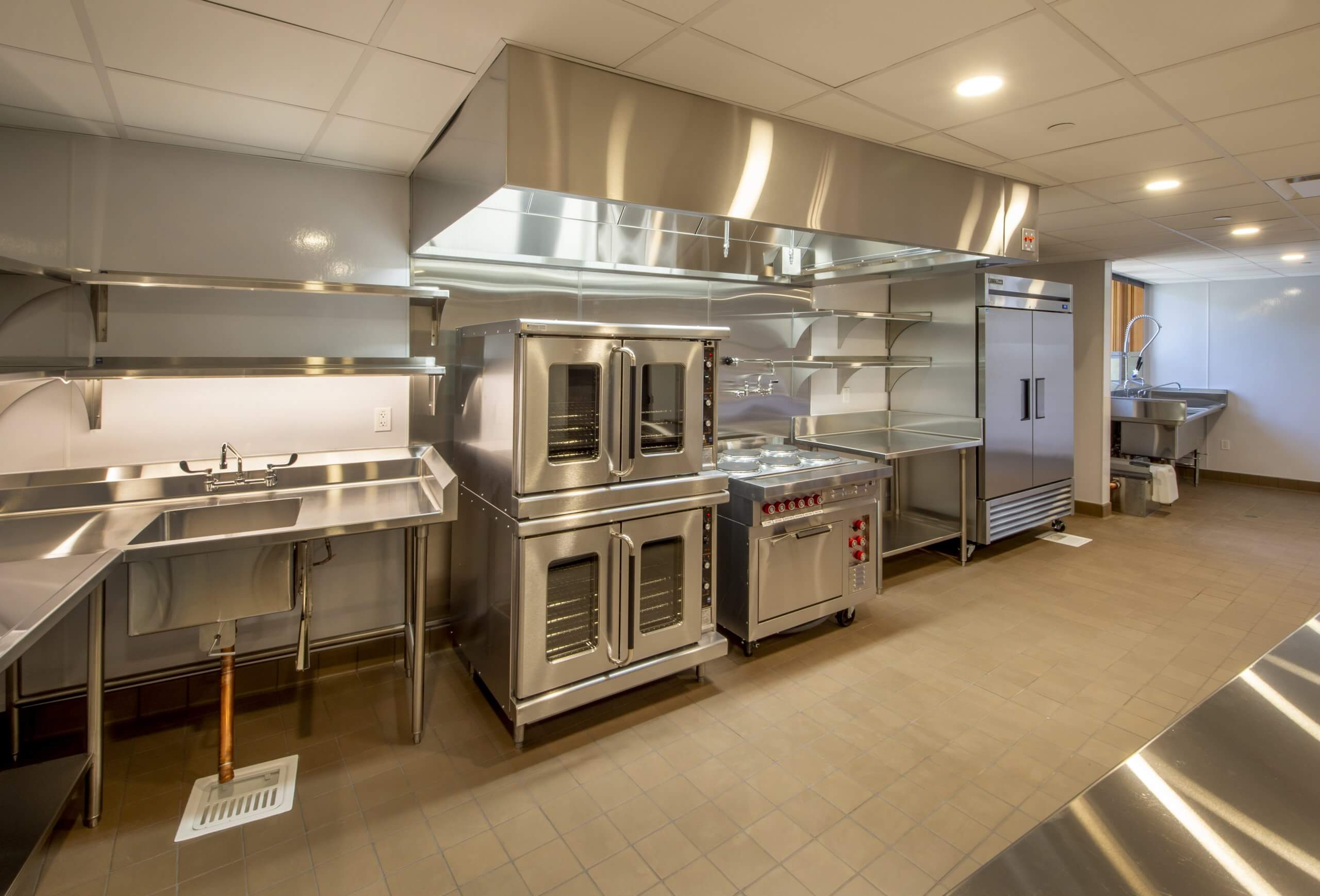 Part of an empty, immaculate industrial kitchen featuring stainless steel appliances.